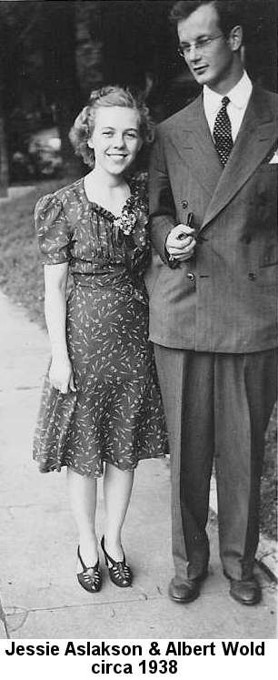 Black and white photo of Jessie Aslakson, a slight young woman in a thin printed knee-length dress with corsage at the neckline, high-heeled sandals, and hair pulled back with ribbons, her left arm around the back of Albert Wold, a tall man with wire-rim glasses, thick dark hair parted on the left with a pompadour, wearing a pin-striped baggy double-breasted suit jacket with wide lapels and polka-dot tie, holding a pipe in his right hand. She is smiling at the camera; he is gazing downward at her lovingly.